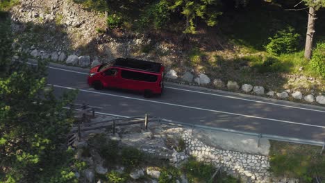 Red-minivan-reveals-from-behind-trees-driving-a-mountain-road-through-forest