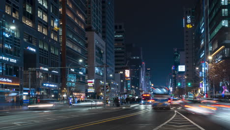Zeitraffer-Der-Geschäftigen-Gangnam-Bushaltestelle-Bei-Nacht-Mit-Einer-Reihe-Von-Bussen,-Die-Nacheinander-In-Der-Mitte-Des-Breiten-Boulevards-In-Der-Innenstadt-Von-Seoul-Und-Hohen-Geschäftstürmen-An-Der-Straße-Vorbeifahren