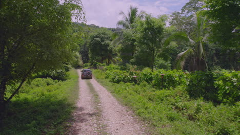 Drone-shot-of-car-driving-on-rural-road-in-the-jungle