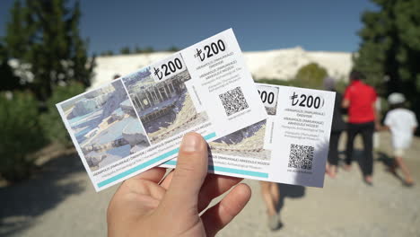 Hand-Holding-Two-Tickets-in-Front-of-Entrance-to-Pamukkale,-Turkey,-First-Person-Point-of-View