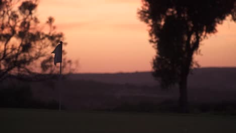 Establishing-view-of-a-flag-waving-in-the-middle-of-a-golf-court-during-golden-hour
