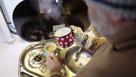 Man-preparing-coffee-in-campervan-kitchen,-top-down-view-of-pouring-hot-boiling-water-into-mug