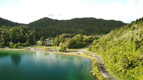Feriencampingplatz-Am-See,-Blauer-See,-Palmenwaldstraße-Und-Tourist-Auf-Paddelbord-4k-drohnenaufnahme-In-Neuseeland
