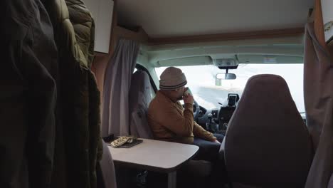 Man-sitting-in-campervan-and-drinking-cup-of-coffee-or-tea,-interior-wide-angle-view