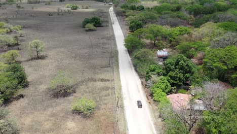Grey-vehicle-turning-right-on-dirt-road-junction-in-Costa-Rica-with-truck-passing-left,-Aerial-dolly-follow-behind-shot