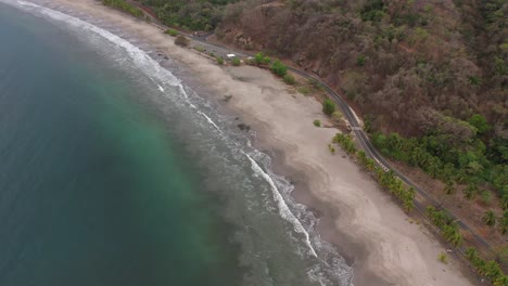Beach-coastline-of-Costa-Rica-with-soft-waves-hitting-rocks-on-sandy-shore,-Aerial-flyover-tilt-down-shot