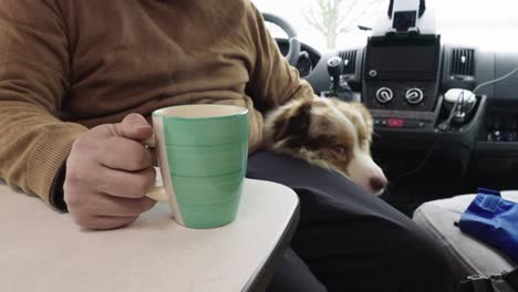 Senior-man-petting-dog-in-campervan,-cup-of-tea-or-coffee-on-table,-interior-view
