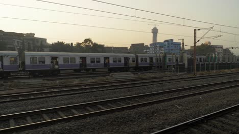 View-of-railway-yard-from-a-moving-train-slowly-leaving-junction-while-other-local-train-standing-and-waiting-for-signal-on-other-line-with-old-rustic-buildings-at-background