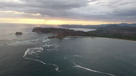 Approaching-coastline-of-Costa-Rica-from-the-Pacific-Ocean-at-sunset-with-rocky-peninsula,-Aerial-flyover-shot
