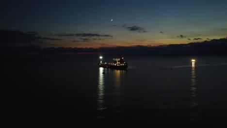 Oil-tanker-at-night,-ascending-aerial-approaching-boat-at-dusk
