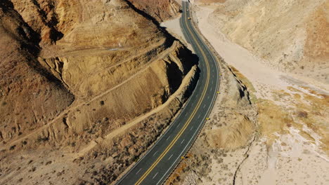 A-highway-winding-through-rugged-desert-terrain---aerial-tilt-up-reveal