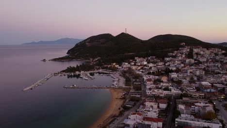 Aerial-approaching-hill-with-telecommunications-antenna-at-dusk-in-small-sea-side-town
