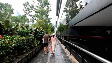 Behind-People-Walking-Along-Modern-Train-in-Narrow-Lush-Street,-Sinapore
