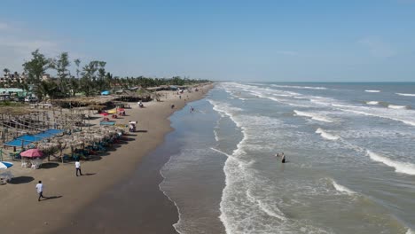 Flying-over-the-palapas-and-unrecognizable-tourists-on-the-beach-at-Tecolutla,-Veracruz-Mexico