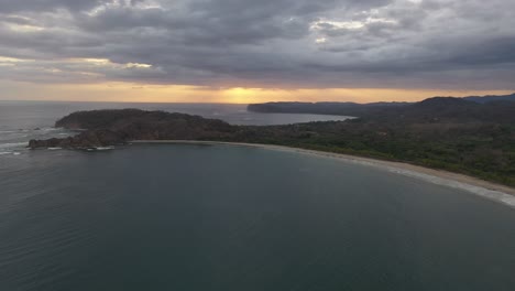 Pacific-Ocean-coastline-of-Costa-Rica-at-sunset-with-sandy-half-moon-beach,-Aerial-flyover-shot