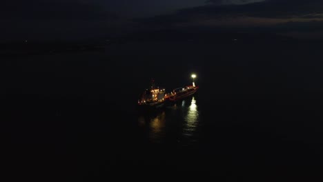 Aerial-pulling-back-over-oil-tanker-in-sea-at-night,-industry,-environment-concept