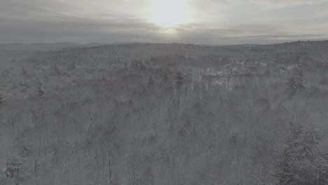 Aerial-view-above-snow-covered-forest-sunlight-breaks-through-clouds