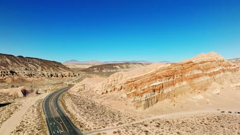 A-desert-highway-with-sandstone-cliffs-and-buttes-on-both-sides---sliding-aerial-view