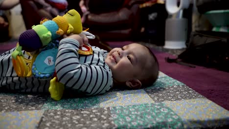Entzückender-4-Monate-Alter-Indischer-Junge,-Der-Auf-Einer-Matte-Auf-Dem-Boden-Liegt-Und-Ein-Sensorisches-Spielzeug-Der-Raupe-Spielt