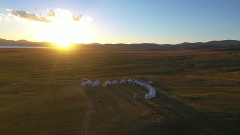 Luftaufnahme-Von-Jurten-Am-Ufer-Des-Song-Kul-Sees,-Wenn-Die-Sonne-über-Der-Weiten-Wildnis-Kirgisistans-Untergeht