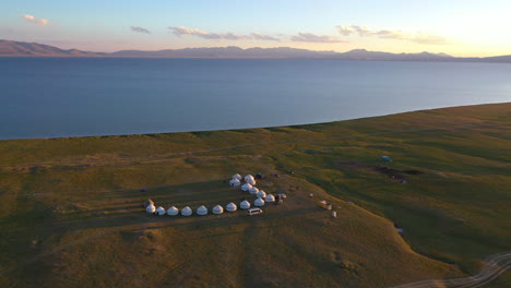 Jurten-Säumen-Das-Ufer-In-Einer-Atemberaubenden-Luftaufnahme-Des-Sonnenuntergangs-über-Dem-Song-Kul-See,-Kirgisistan