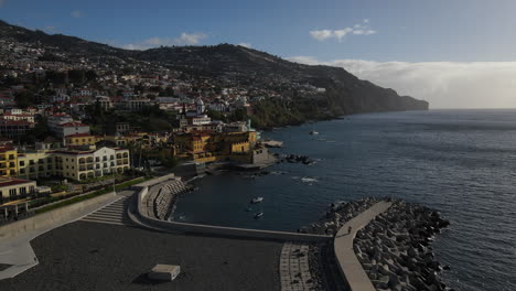 Toma-Aérea-Sobre-El-Muelle-Del-Puerto-De-Funchal-Y-Acercándose-Al-Fuerte-De-Madeira-Y-Donde-Se-Pueden-Ver-Las-Muchas-Casas-Y-Edificios-De-La-Costa