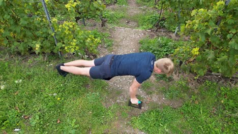 aerial,-a-young-athlete-does-push-ups-in-a-vineyard,-Lavaux,-Switzerland,-exercising