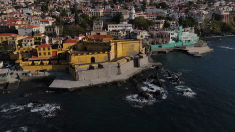 Aerial-shot-in-a-circle-of-the-Madeira-fort-in-the-city-of-Funcal-and-where-the-houses-and-buildings-of-the-coast-can-be-seen
