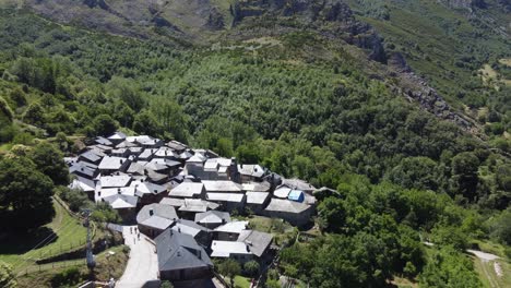 Aerial-view-of-stone-village-with-slate-roofs-surrounded-by-green-mountains