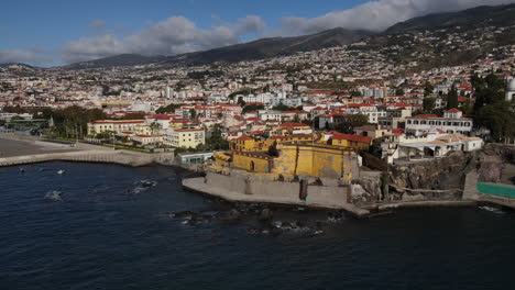 aerial-shot-in-distance-of-the-Madeira-fort-in-the-city-of-Funcal-and-where-the-houses-and-buildings-of-the-coast-can-be-seen