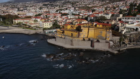 Aerial-shot-in-a-circle-of-the-Madeira-fort-in-the-city-of-Funchal-and-where-you-can-see-the-many-houses-and-buildings-on-the-coast