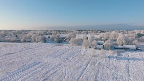 Aerial-establishing-view-of-a-rural-landscape-in-winter,-snow-covered-countryside-fields-and-trees,-cold-freezing-weather,-sunny-winter-day-with-blue-sky,-wide-drone-shot-moving-forward
