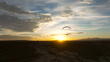 Silhouette-of-a-powered-paraglider-flying-into-a-golden-sunset-over-the-Mojave-Desert