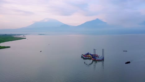 Drone-shot-of-dredger-boat-with-excavator-on-the-beautiful-lake-with-mountain-on-the-background