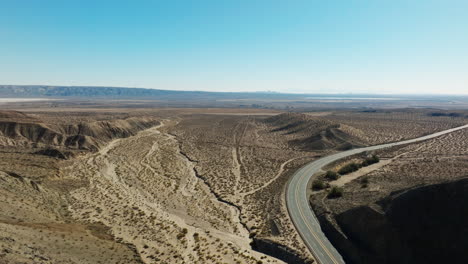 The-Mojave-Desert-with-Highway-58-passing-through-its-arid-landscape-on-a-clear-day---aerial-pull-back
