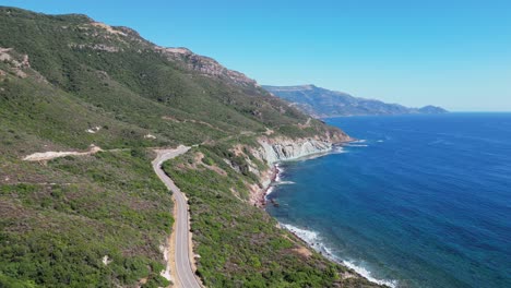Coastal-Road-between-green-mountains-and-blue-sea-in-Sardinia,-Italy---4k-Aerial