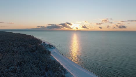 Aerial-establishing-footage-of-trees-covered-with-snow,-sunny-winter-day-at-the-sunset,-golden-hour,-Nordic-woodland-pine-tree-forest,-Baltic-sea-coast,-wide-drone-shot-moving-forward