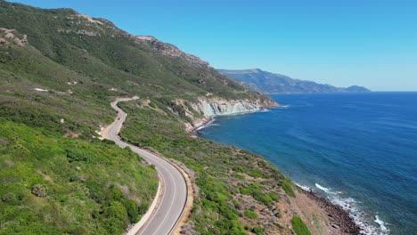 Coastal-Road-between-green-mountains-and-blue-sea-in-Sardinia,-Italy---4k-Aerial-Pedestal