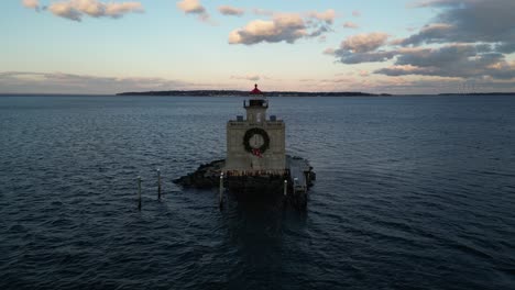 An-aerial-view-of-the-Huntington-Harbor-Lighthouse-on-Long-Island,-NY-at-sunset,-with-a-Christmas-wreath