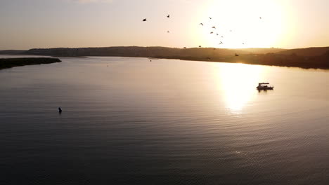 Filmische-Sonnenuntergangsantenne-Der-Bootssilhouette-In-Gold-Und-Gelber-Reflexion-In-Der-Flussmündungsoberfläche-Des-Keurbooms,-Vorbeifliegende-Wasservögel