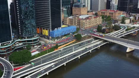 Brisbane-city-development,-aerial-view-overlooking-at-m3-pacific-motorway-riverside-expressway,-tilt-up-reveals-treasury-casino-heritage-building-and-queen's-wharf-construction-in-progress-in-downtown