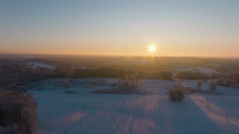 Aerial-establishing-view-of-a-rural-landscape-in-winter,-snow-covered-countryside-fields,-cold-freezing-weather,-sunset-with-golden-hour-light,-wide-drone-shot-moving-forward