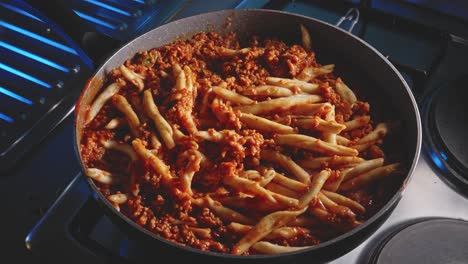 Static-close-up-of-a-hot-steaming-vegetarian-bolognese-with-fileja-pasta-cooking-in-a-nonstick-frying-skillet-pan-on-a-cooktop-stove-with-cinematic-dual-tone-lighting,-slow-zoom-in
