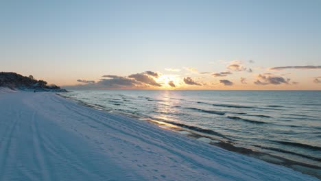 Aerial-footage-of-beach-covered-with-snow,-sunny-winter-day-at-the-sunset,-golden-hour,-Nordic-woodland-pine-tree-forest,-Baltic-sea-coast,-wide-drone-shot-moving-forward-low