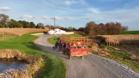 Aerial-drone-shot-of-children-enjoying-farm-hayride-on-wagon-pulled-by-tractor-during-autumn-fall-harvest-season
