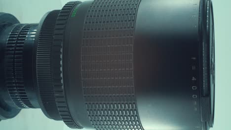Cinematic-Vertical-Close-up-shot-of-a-400mm-metal-tele-macro-lens,-camea-optical-equipment,-360-rotating-stand,-product-video,-slow-motion,-4K