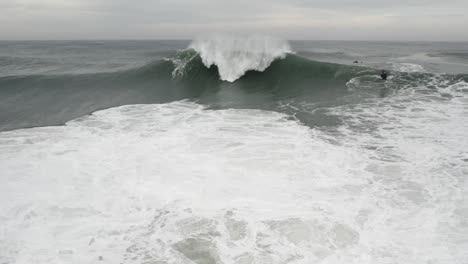 Slow-motion-shot-of-Big-ocean-wave-breaking-and-splashing-sea-foam-on-overcast-day,-Nazare