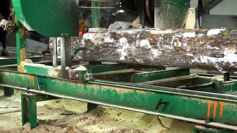 Sawing-timber-in-sawmill-with-a-stationary-bandsaw,-closeup-pan-right