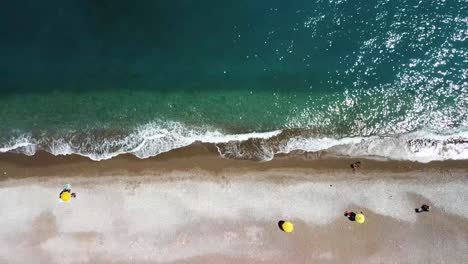 Aerial-view-of-yellow-umbrellas-on-a-beach-with-crystal-clear-waters