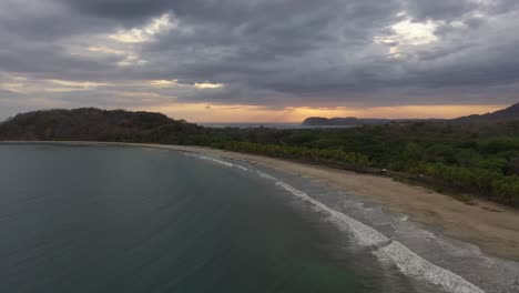 Coastline-of-Nosara-Beach-Costa-Rica-Playa-Pelada-with-soft-waves-on-sandy-shore-at-sunset,-Aerial-flyover-shot